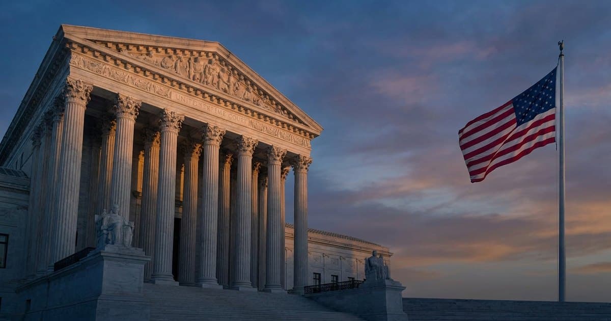 The United States Supreme Court building at dusk with an American flag