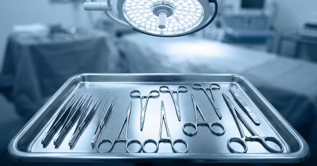 A sterile stainless-steel surgical instrument tray under an operating light