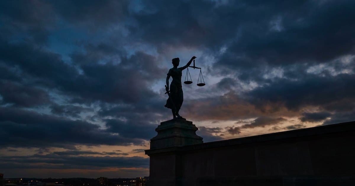 A bronze statue of Lady Justice holding balanced scales against a dusk sky
